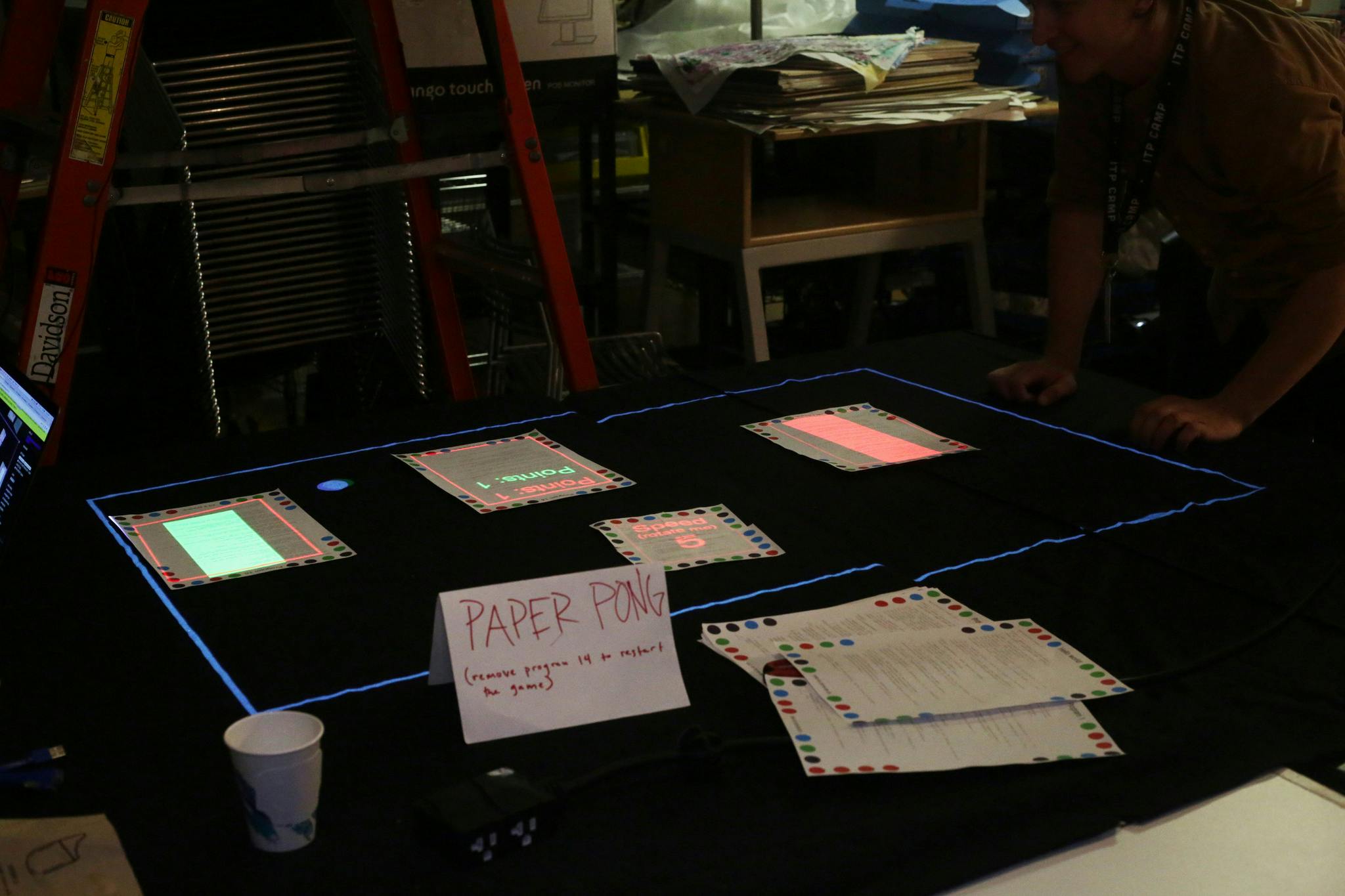 A projection-mapped game of pong played with pieces of paper